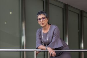 Image shows gray-haired person in flowy top leaning on a railing.