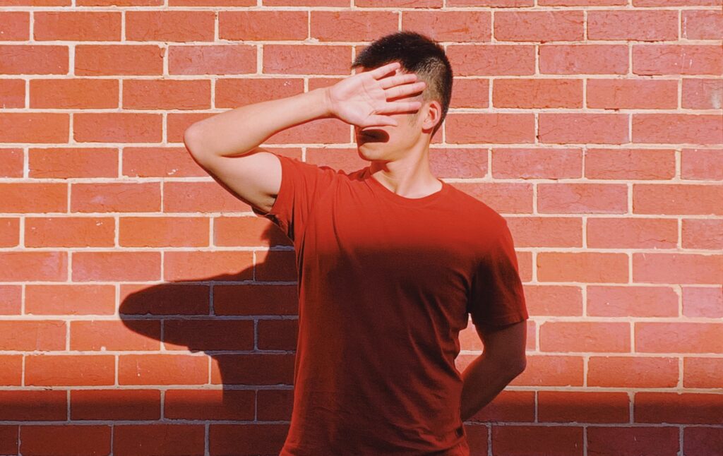 Helping Your Clients Reclaim Their Voice. Image shows person standing in front of brick wall, head turned away, hand up blocking their face.