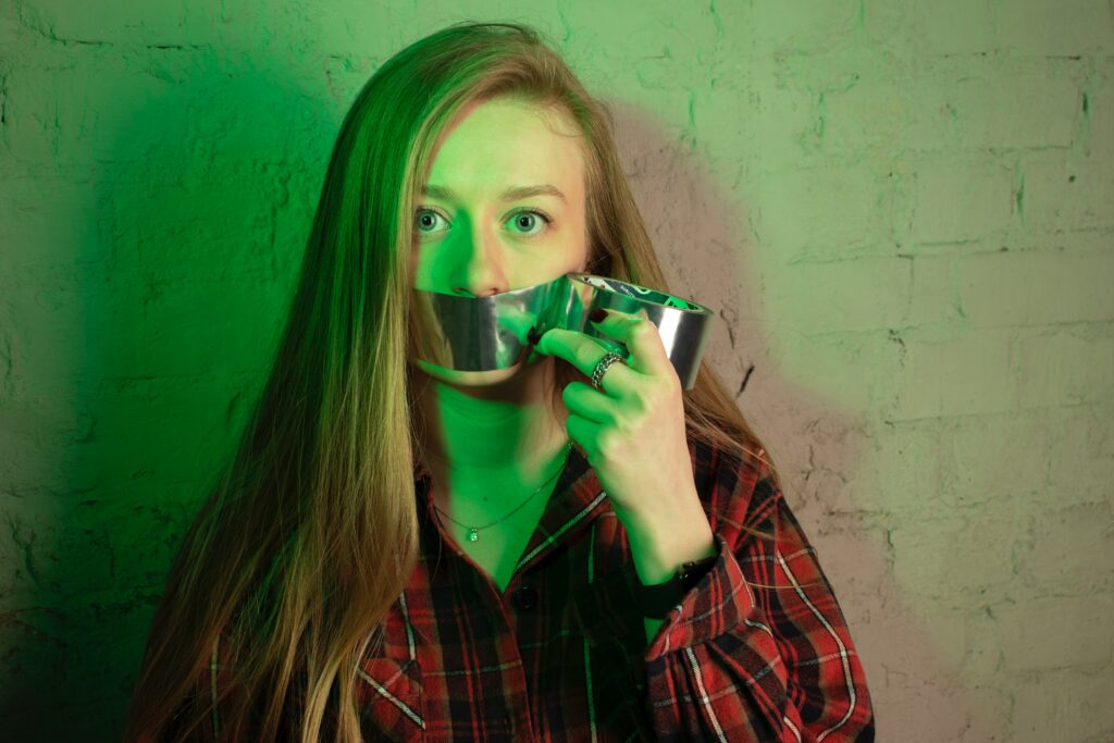 Helping Clients Reclaim Their Voice. Image shows person putting duct tape on their own mouth.