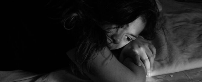 Woman laying in bed, looking pensive, perhaps experiencing body grief