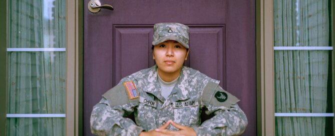 A woman who is part of a military couple sits in front of a door.