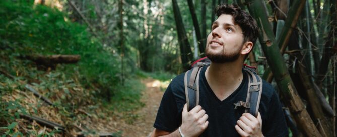 a man hiking with a backpack looking up to the trees in a forest practicing ecosexuality
