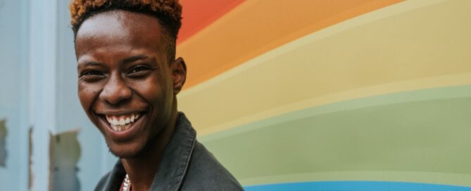 a sex coach becoming a better ally to lgbtq smiles in front of a rainbow backdrop