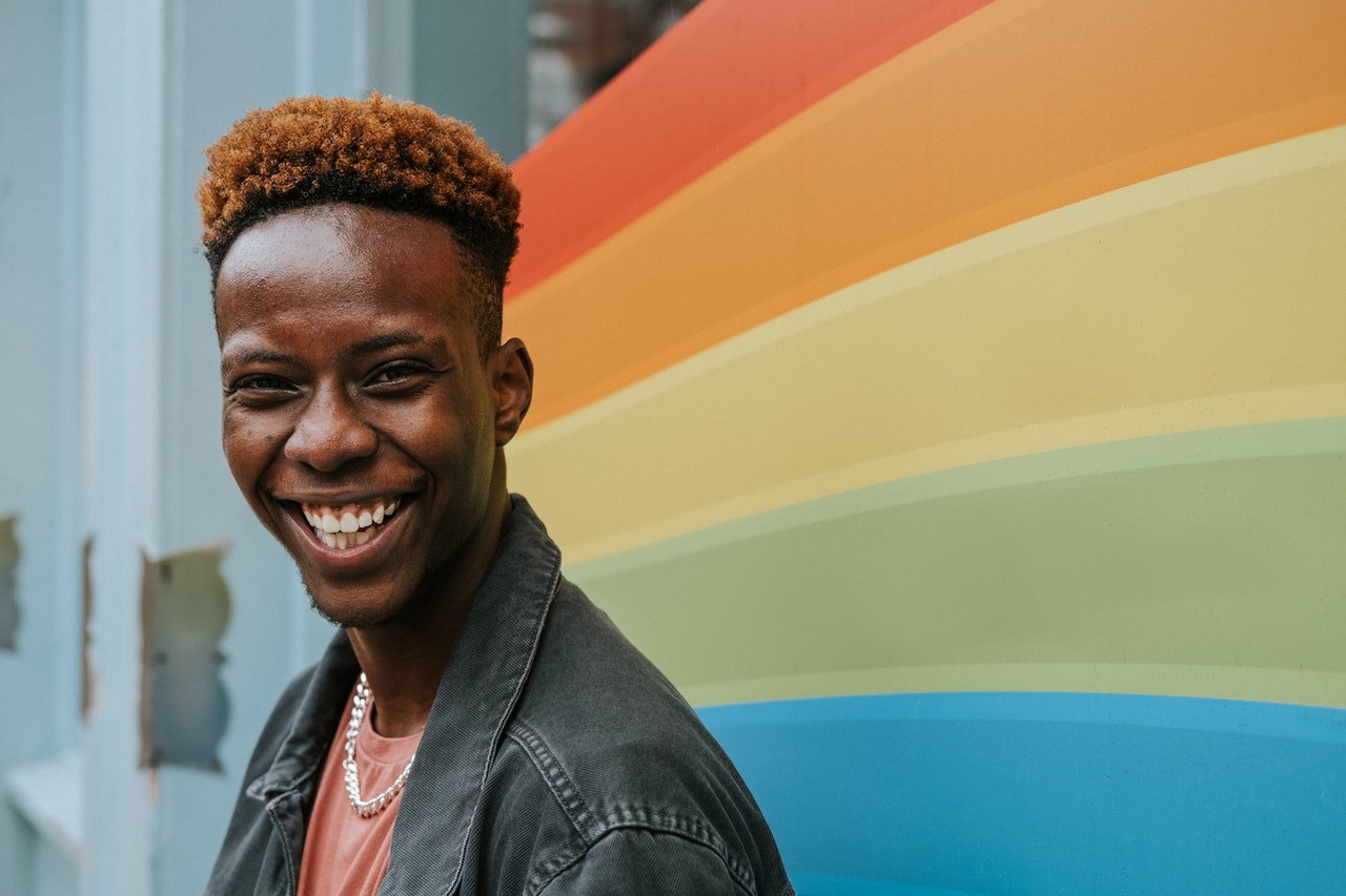 a sex coach becoming a better ally to lgbtq smiles in front of a rainbow backdrop
