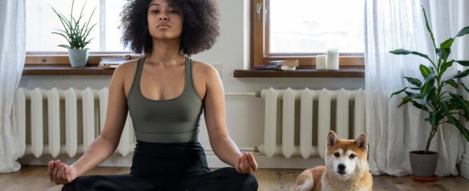 a woman sitting cross legged on a yoga mat with a dog practicing mindfulness for her sex coaching practice