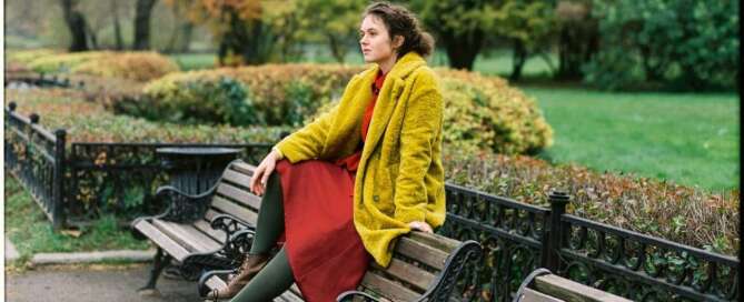 A person in a yellow coat sits on a park bench contemplating the performative gratitude expected during the Thanksgiving holiday.