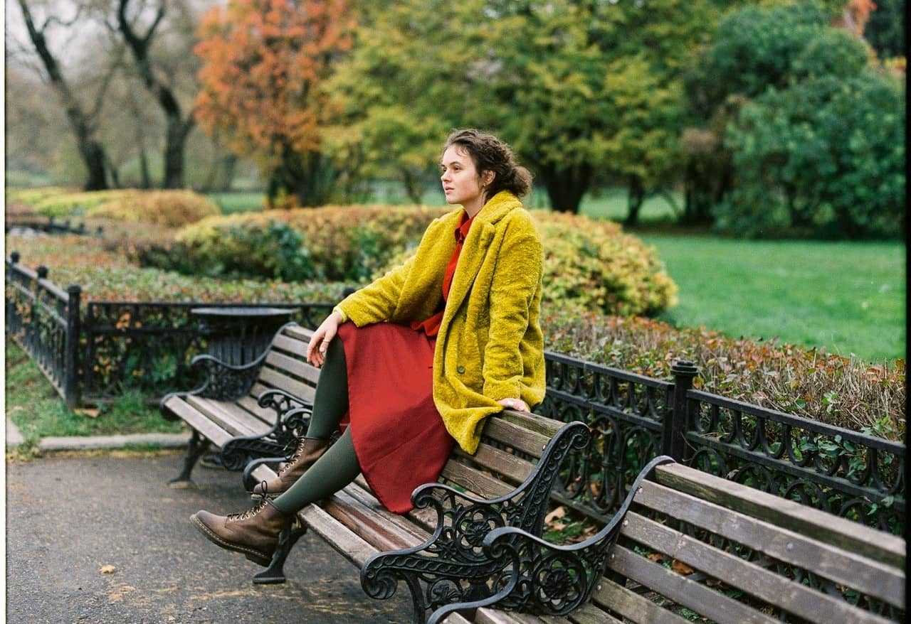 A person in a yellow coat sits on a park bench contemplating the performative gratitude expected during the Thanksgiving holiday.