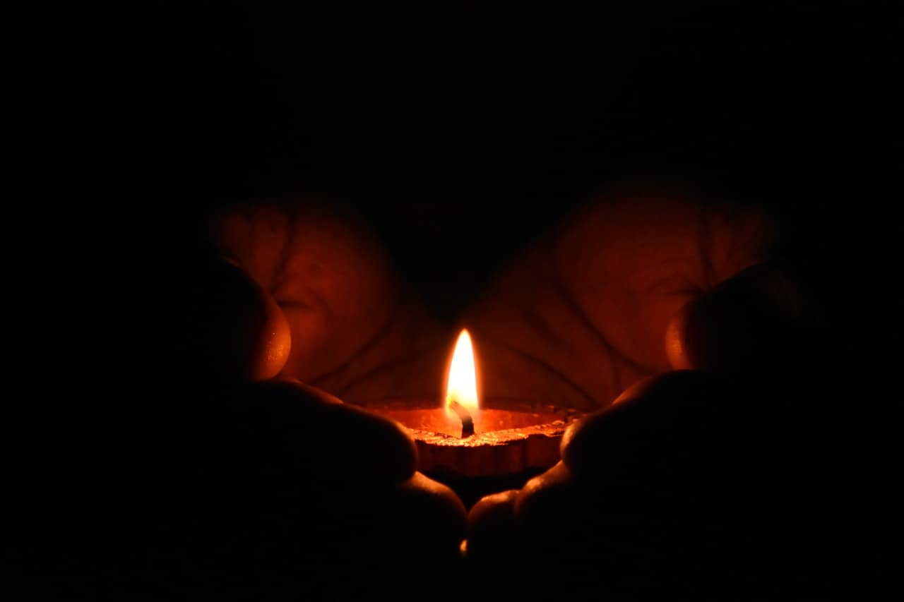 Hands holding a small candle light in darkness representing the Winter Solstice.