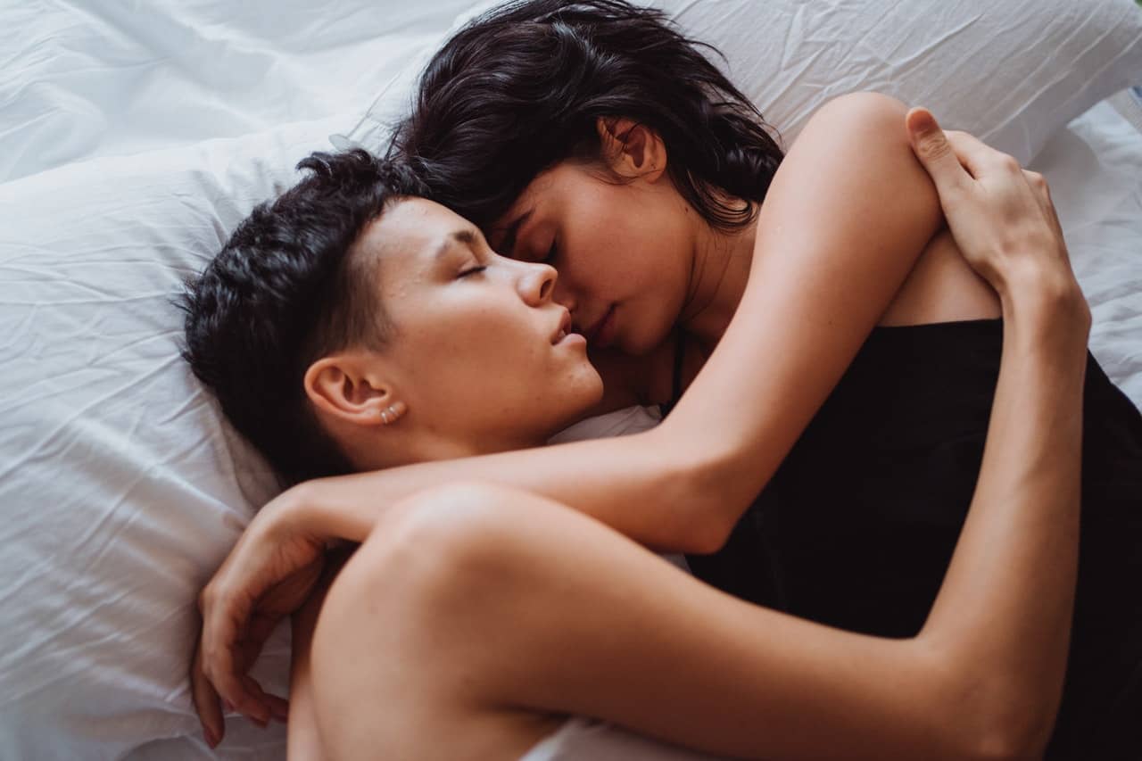 Two women embracing in bed. Women loving women can overcome lesbian bed death.