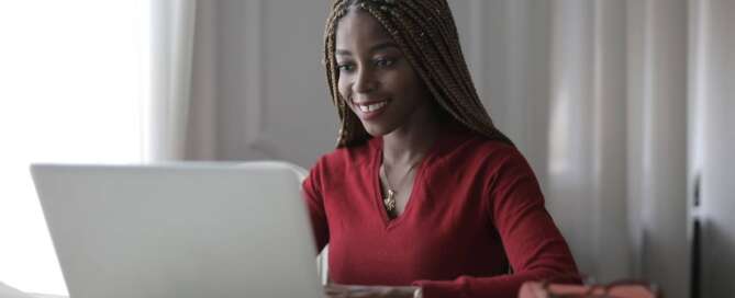 a woman in a red shirt smiling at her laptop as she works to improve her website conversion