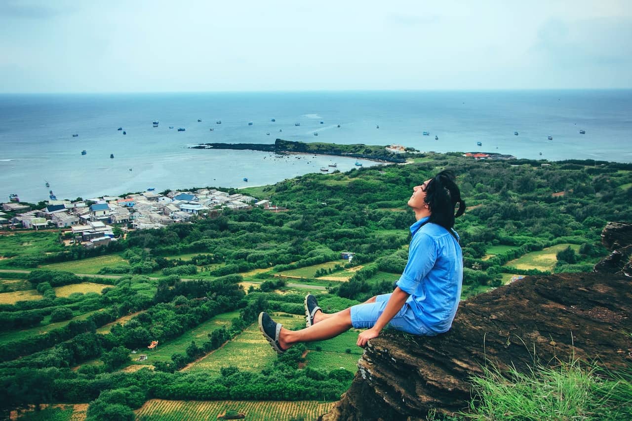 A man sits on the edge of a cliff overlooking a beautiful landscape, embodying freedom after using pleasure products to resolve his sexual concern