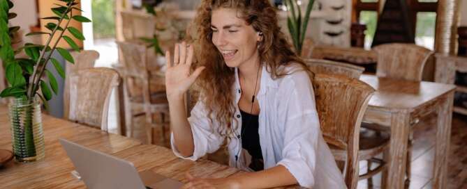 A woman sits in front her laptop waving to a client through the screen, suggesting pleasure products to help them overcome their sexual concern