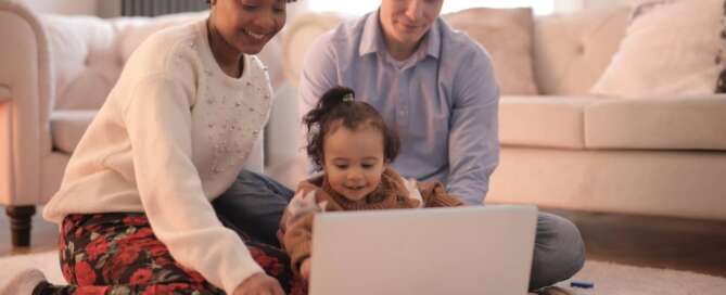 two parents happily sitting with their child looking at a screen