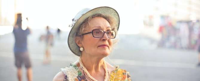 A midlife woman wearing a hat and floral top looks to the side off camera.