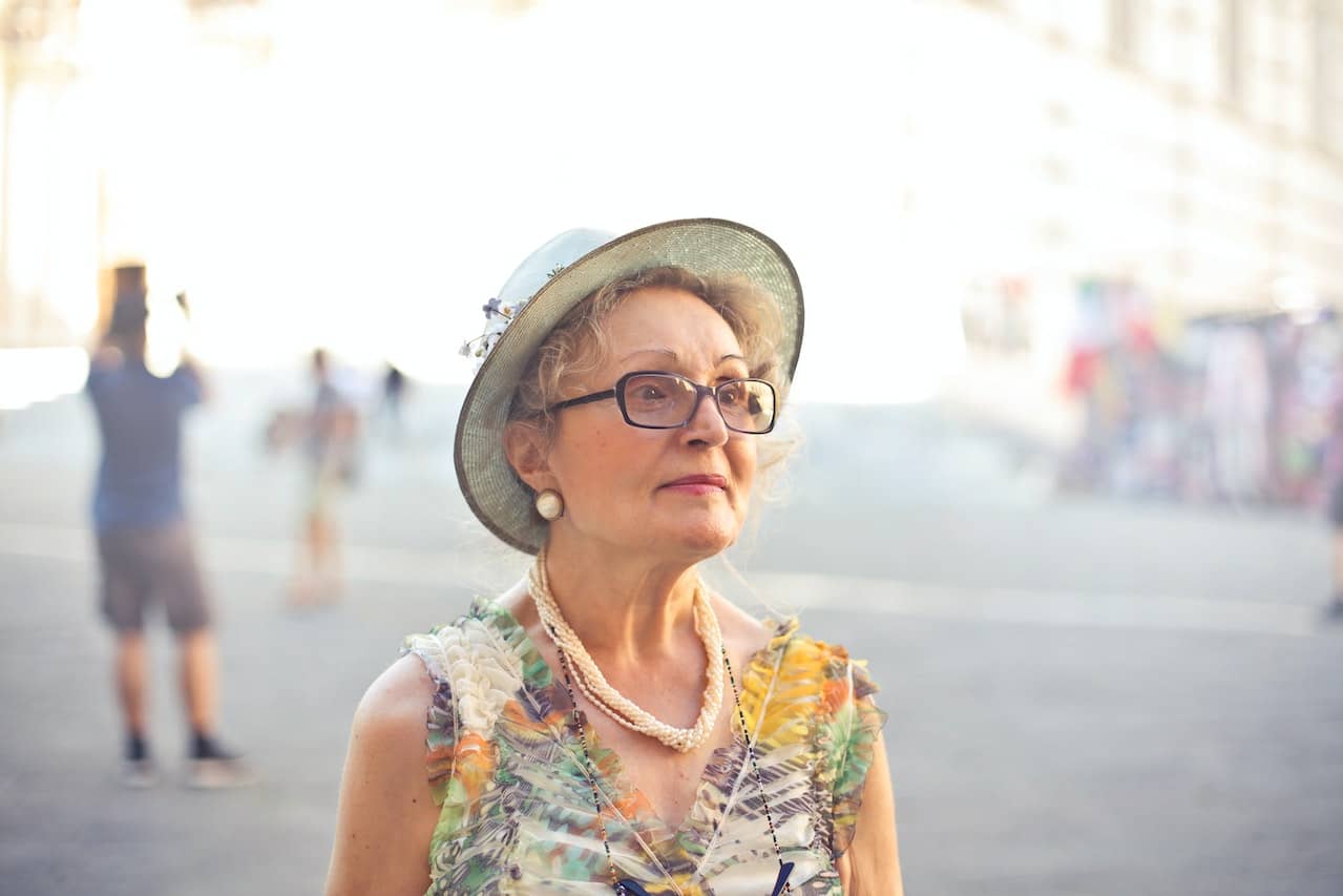 A midlife woman wearing a hat and floral top looks to the side off camera.