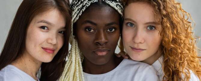 Three women standing close together with their heads touching smile slightly at the camera because they know the world needs more sexological professionals.