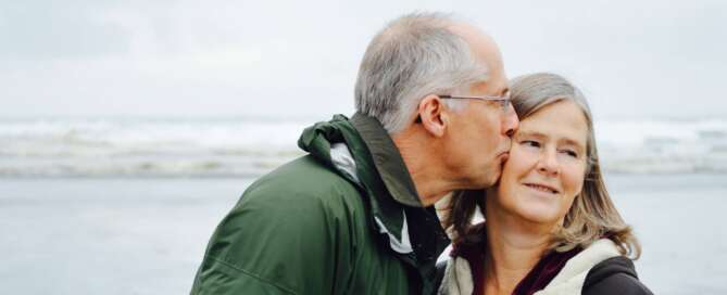 An older couple stands on the beach and embraces each other because they resolved their erectile dysfunction difficulties.