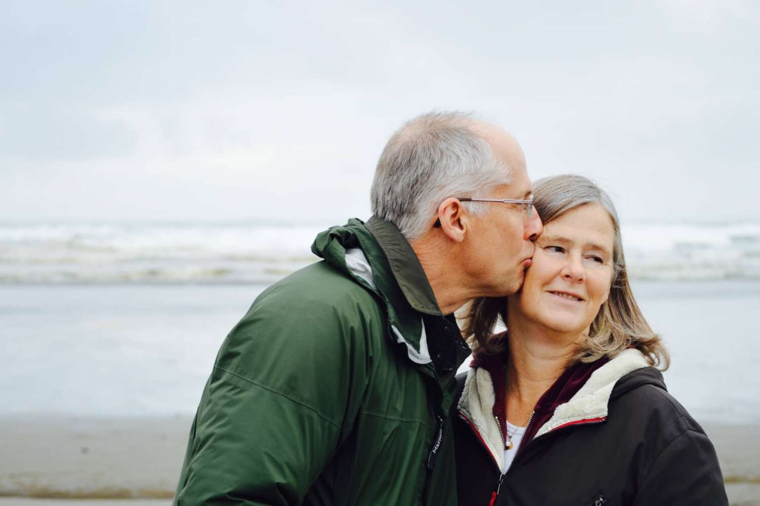 An older couple stands on the beach and embraces each other because they resolved their erectile dysfunction difficulties.
