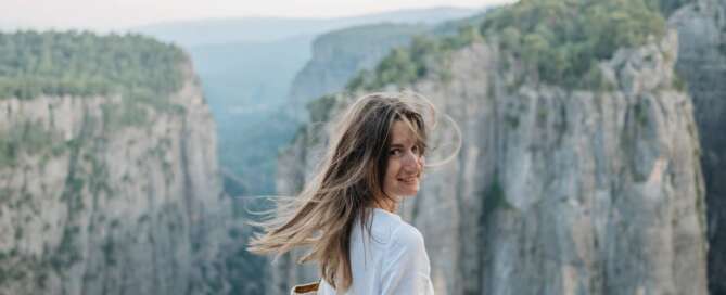 a woman on top of a cliff looks at the camera with wind in her hair smiling because she took the leap into a sex coaching career