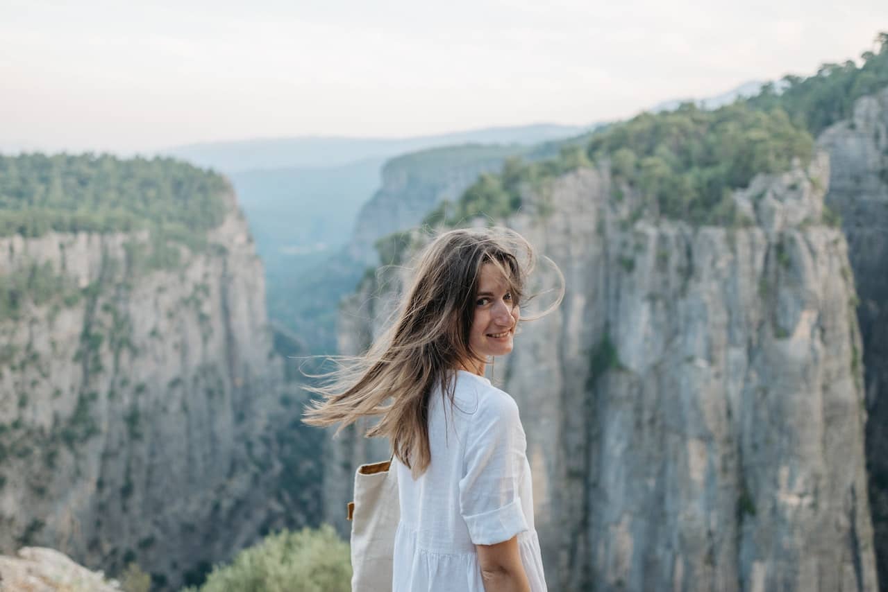 a woman on top of a cliff looks at the camera with wind in her hair smiling because she took the leap into a sex coaching career