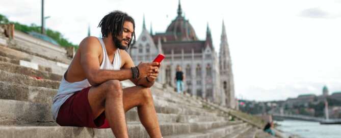 A man sits on stairs looking at his phone with a castle in the background widening his perspective after doing a SAR training