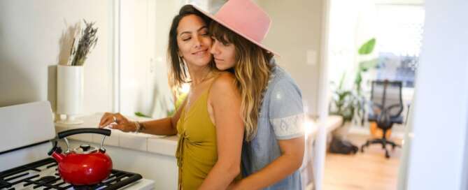 two feminine people stand embracing each other in a kitchen after learning to understand Pansexuality and Panromanticism for Sex Coaches