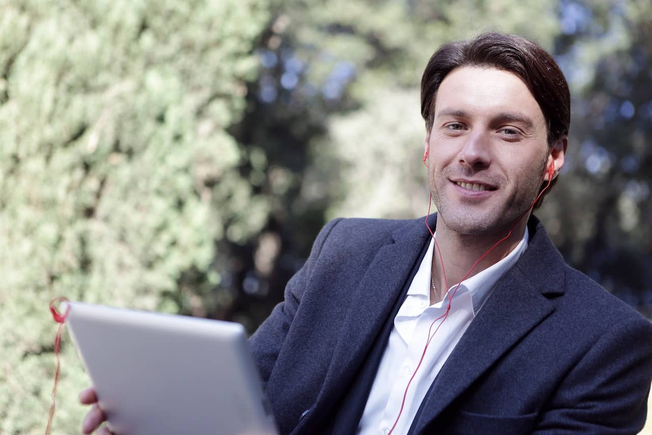a man in a suit wearing wired earbuds and holding a tablet smiles at the camera, pleased because he has learned about the different careers in sexuality