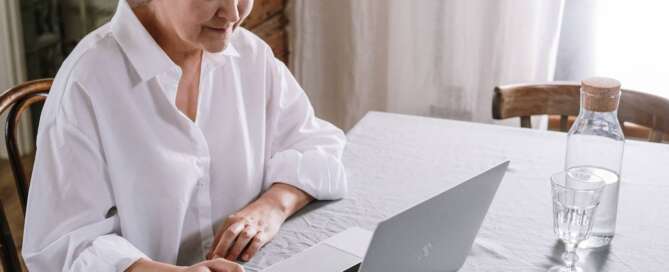 a woman in a white blouse looks at an open laptop while holding a business card in her hand, virtually networking to benefit her client attraction strategy.