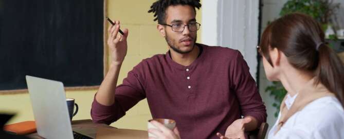 two people sit in front of a laptop and look at each other while speaking about sex coaching for sexual communication.