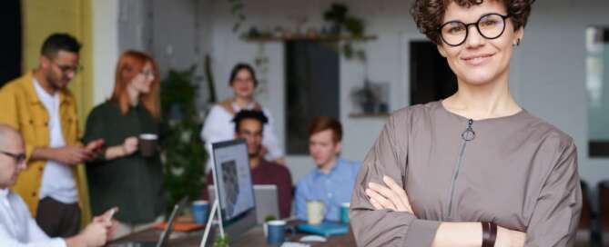 a person stands with arms crossed smiling at the camera, with a team of people working behind them while overcoming social stigma associated with sex in business