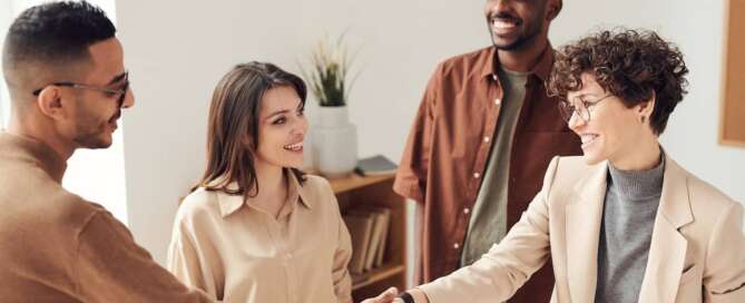 Four people stand around each other while two shake hands after using generative ai to connect with sex coaching clients