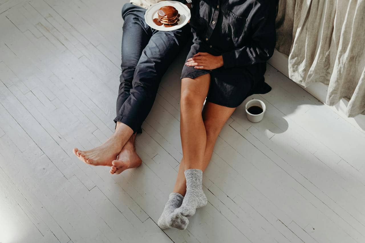 a bird’s eye view of two pairs of legs with a mug of coffee off the side, depicting a couple after experiencing sex coaching