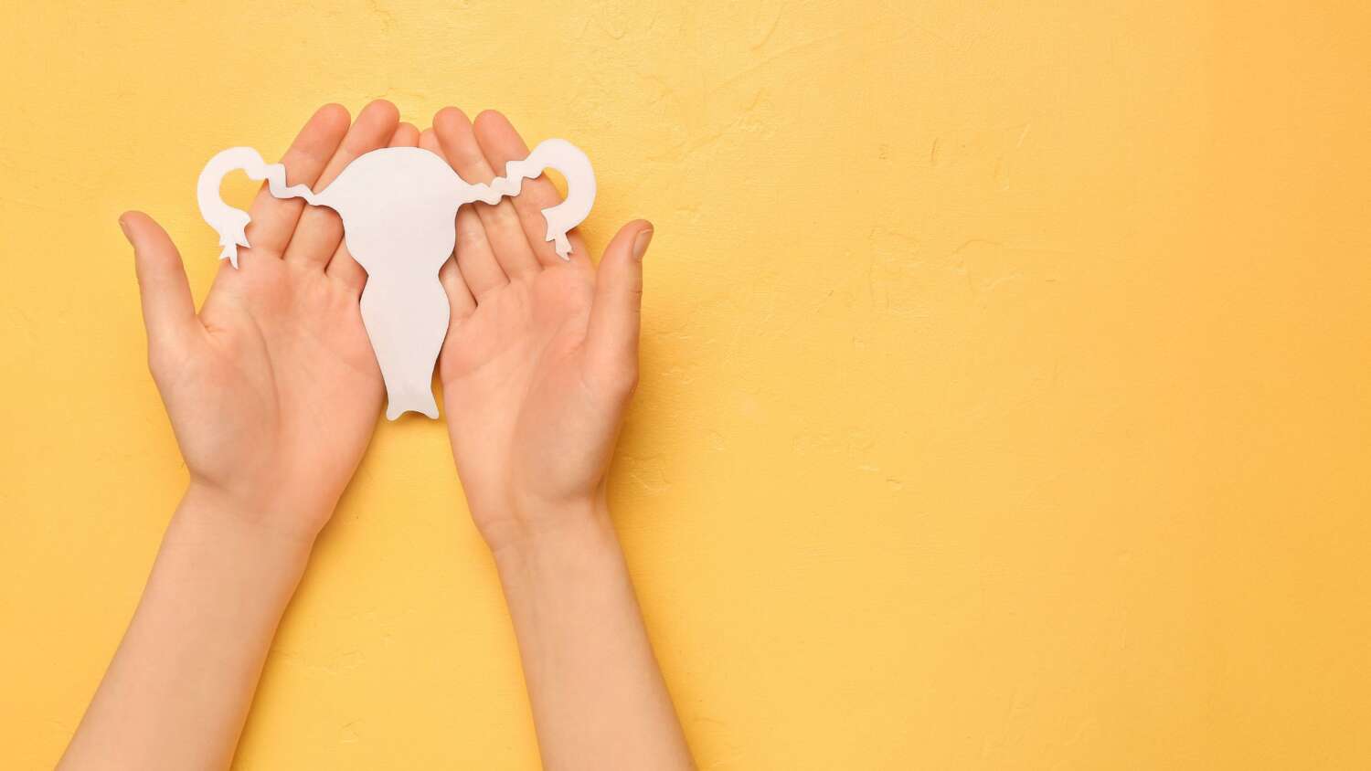 Hand holding paper uterus on yellow background — endometriosis awareness and sexual health